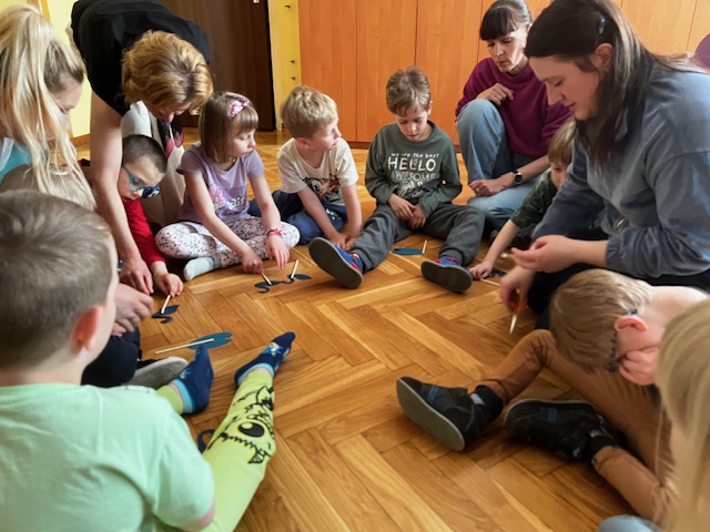 Dzieci siedzą na podłodze i wykonują swoje figurki do teatrzyku cieni.