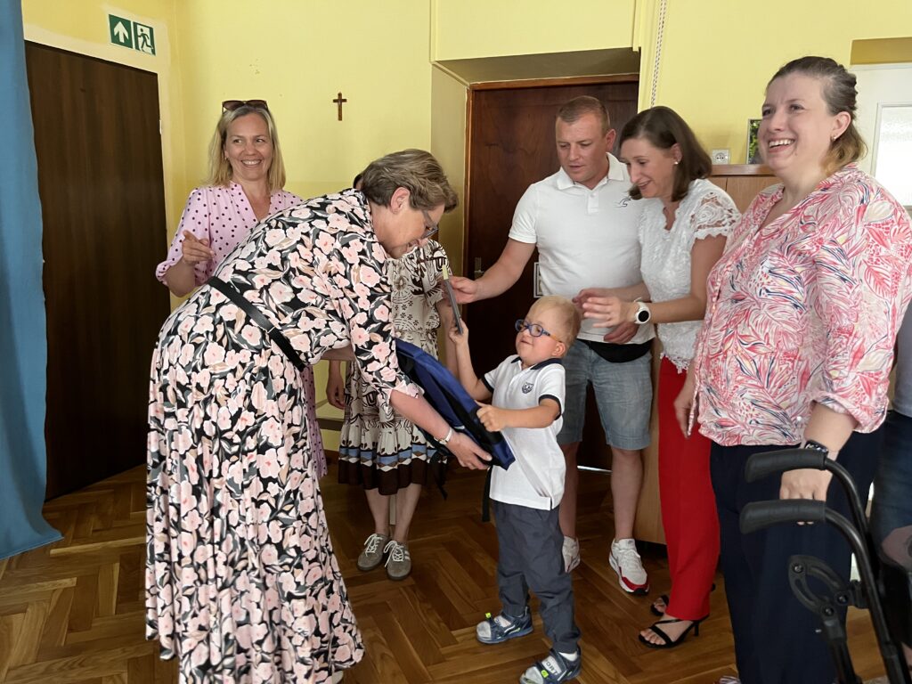 Dyrektor wręcza chłopcu upominek. Wokoło dziecka stoją rodzice i nauczyciel.
