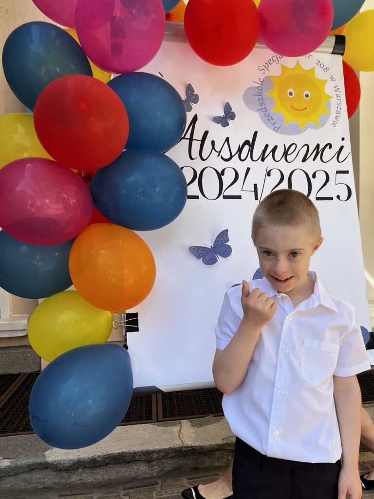 Chłopiec stoi przy tablicy z napisem: Absolwenci 2024/2025