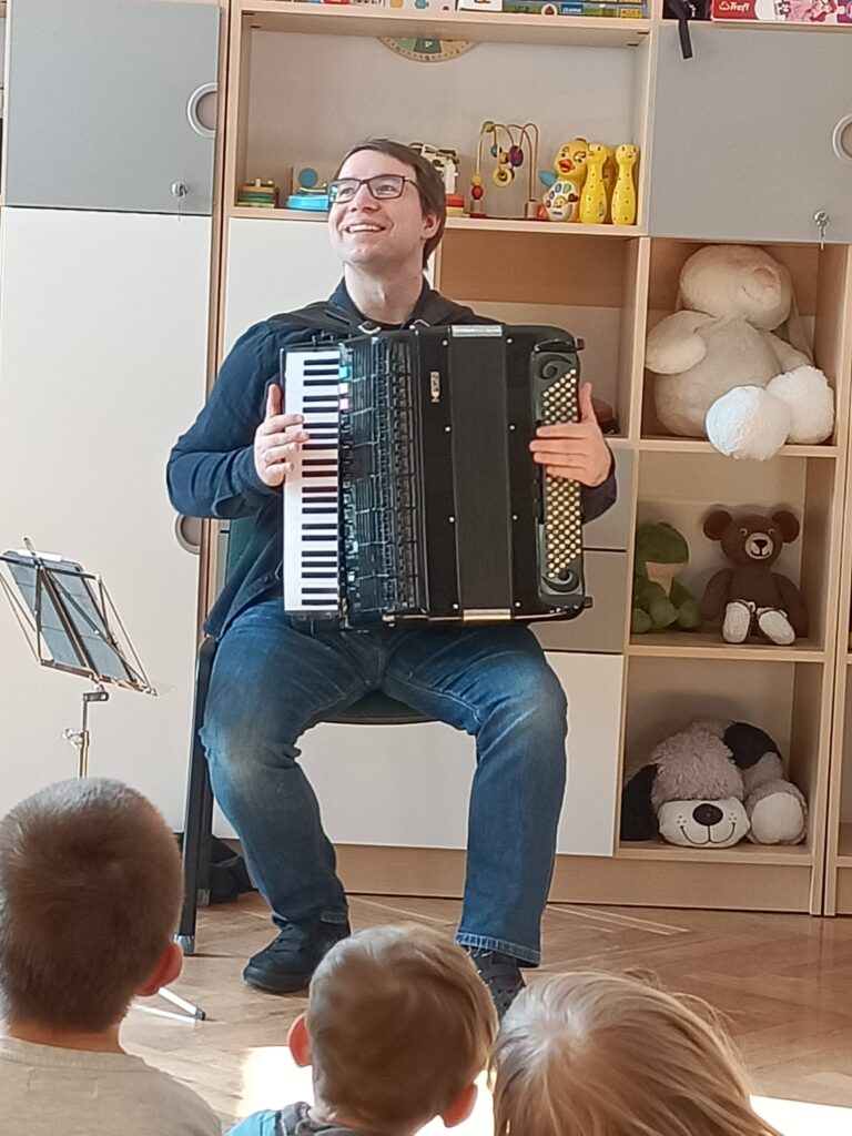 Pan siedzi na krześle i gra na akordeonie.