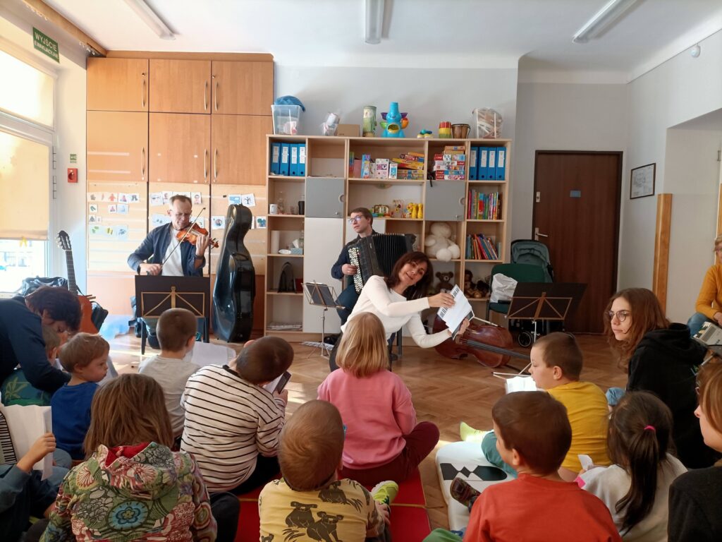 Pani pokazuje dzieciom, jak grać na akordeonie zrobionym z papieru.