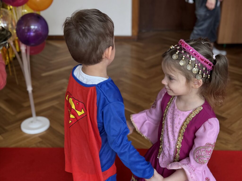 Dziewczynka przebrana za księżniczkę tańczy z chłopcem w stroju Batmana w kółeczku